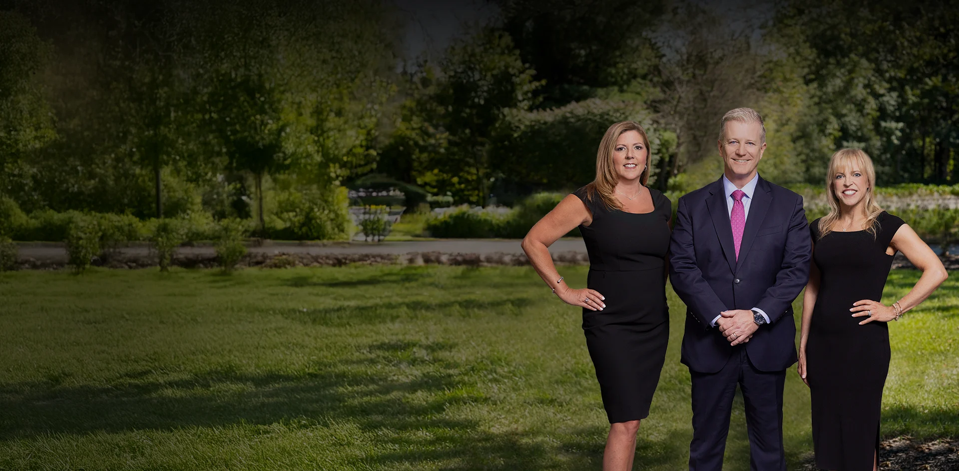 Kaplan, Weinberg, and Smith stand confidently on grass in a garden with trees and flowers.