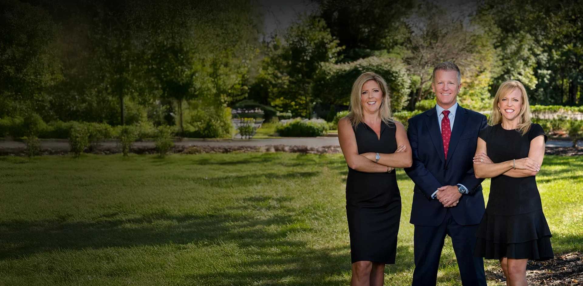 Kaplan, Weinberg, and Smith stand confidently on grass in a garden with trees and flowers.