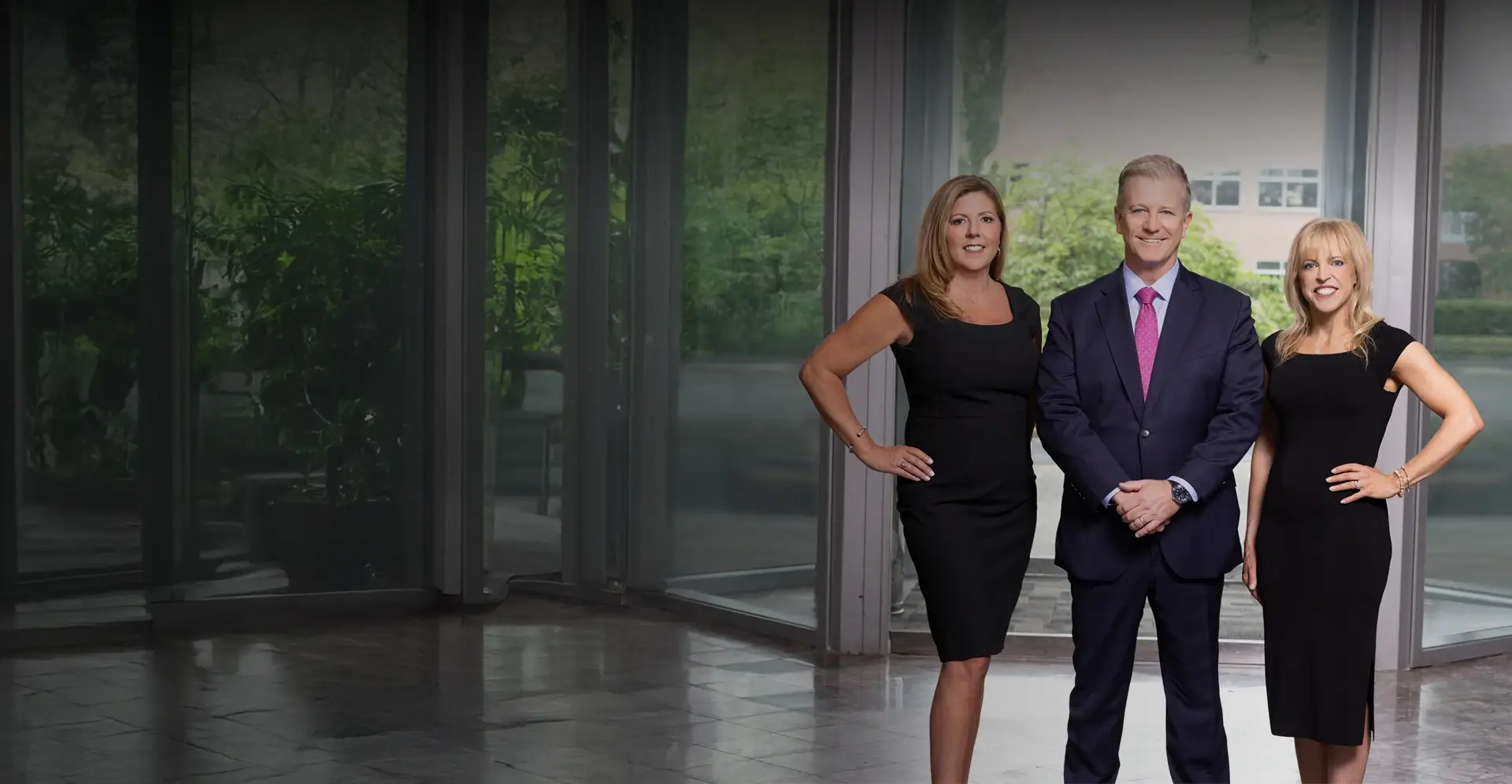 Kaplan, Weinberg, and Smith Attorneys stand confidently on green grass in a garden with trees and flowers.