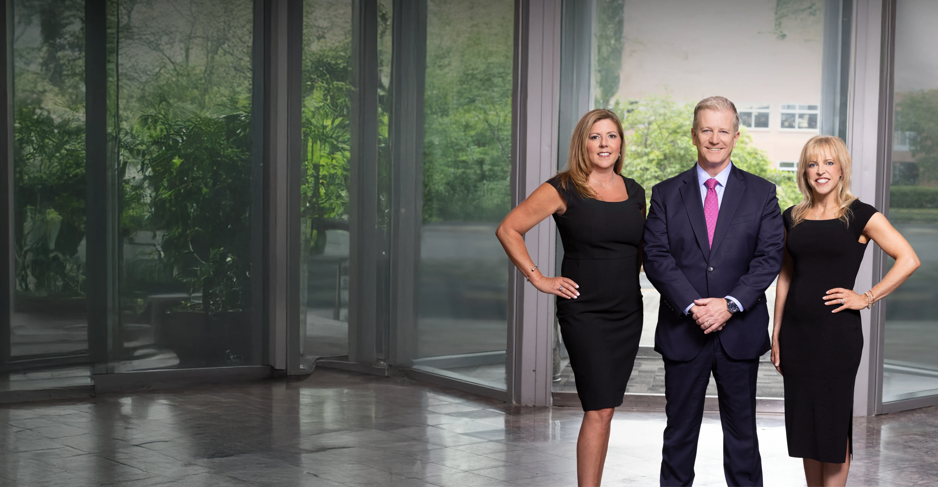 Kaplan, Weinberg, and Smith Attorneys stand confidently on green grass in a garden with trees and flowers.